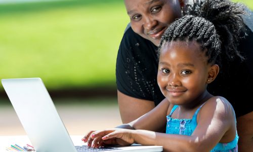 Close up portrait of little african girl with braids and mother with laptop.Kid typing on laptop against green background outdoors.